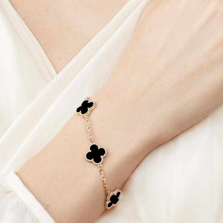 Elegant clover charm bracelet with polished black agate inlays and a gold and silver-tone chain for sophisticated style.