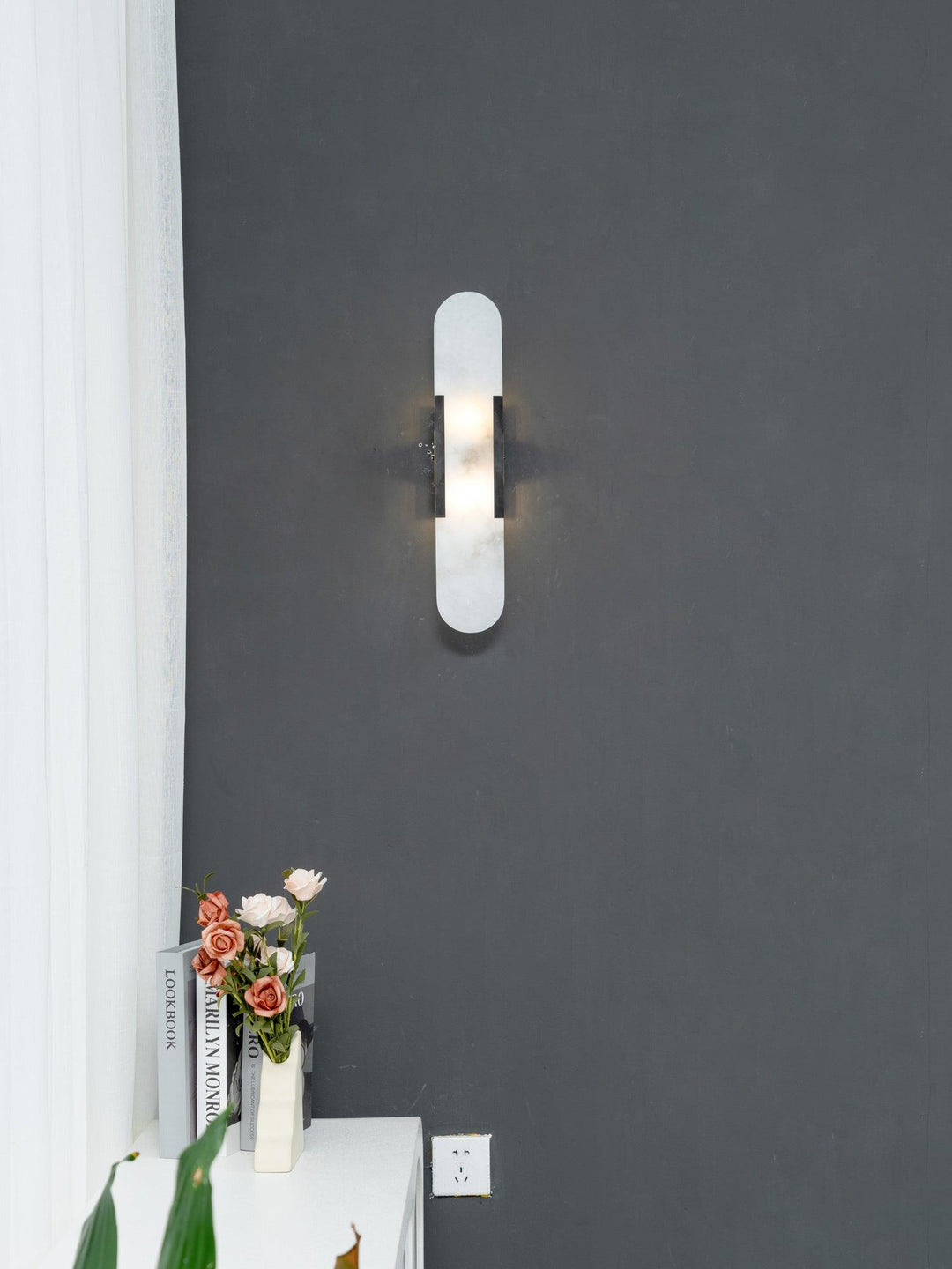 "Modern elongated alabaster wall lamp with metal and brass accents, emits warm glow, suitable for chic interior decor."