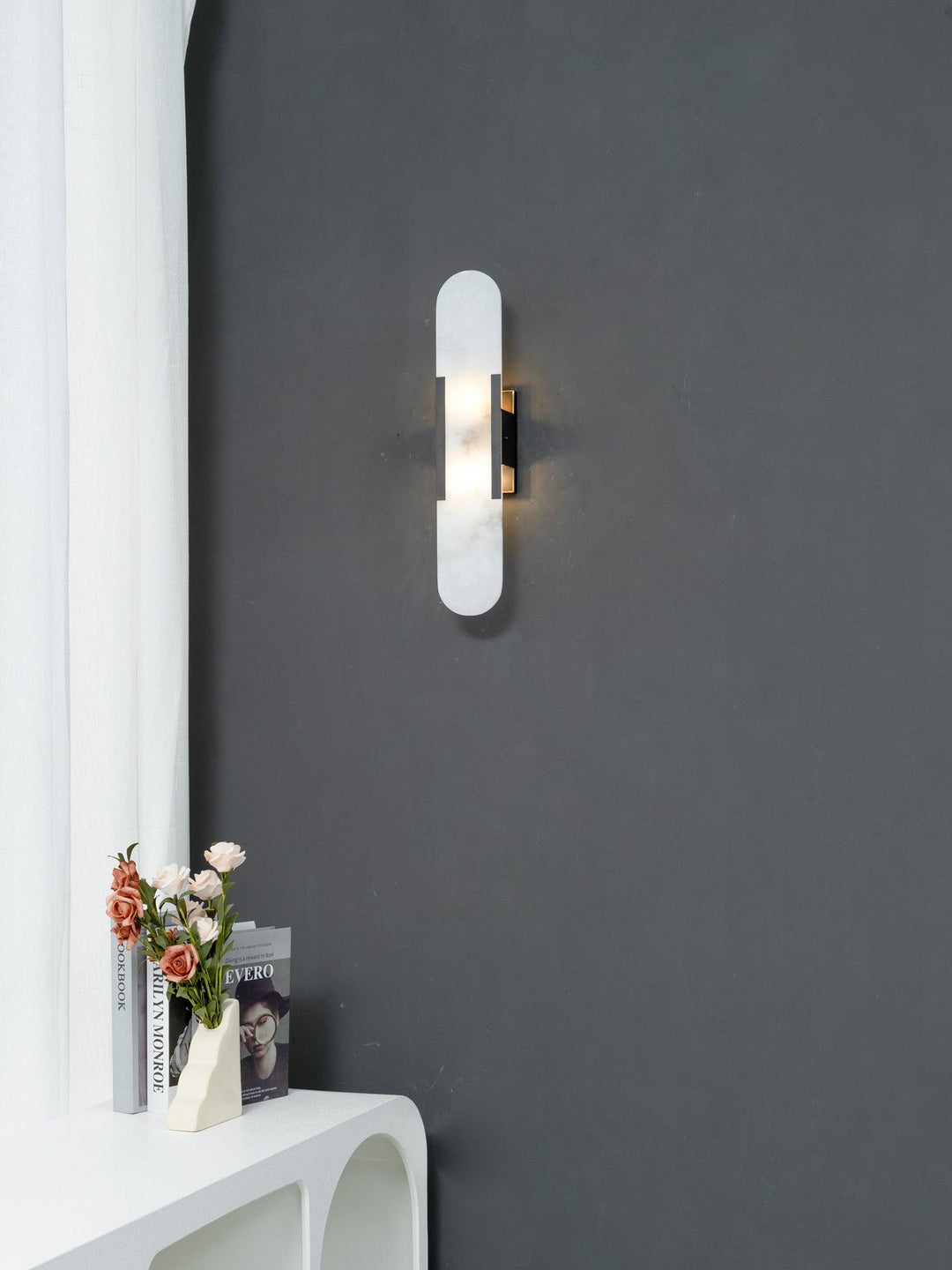 "Modern elongated alabaster wall lamp with metal and brass accents, emits warm glow, suitable for chic interior decor."