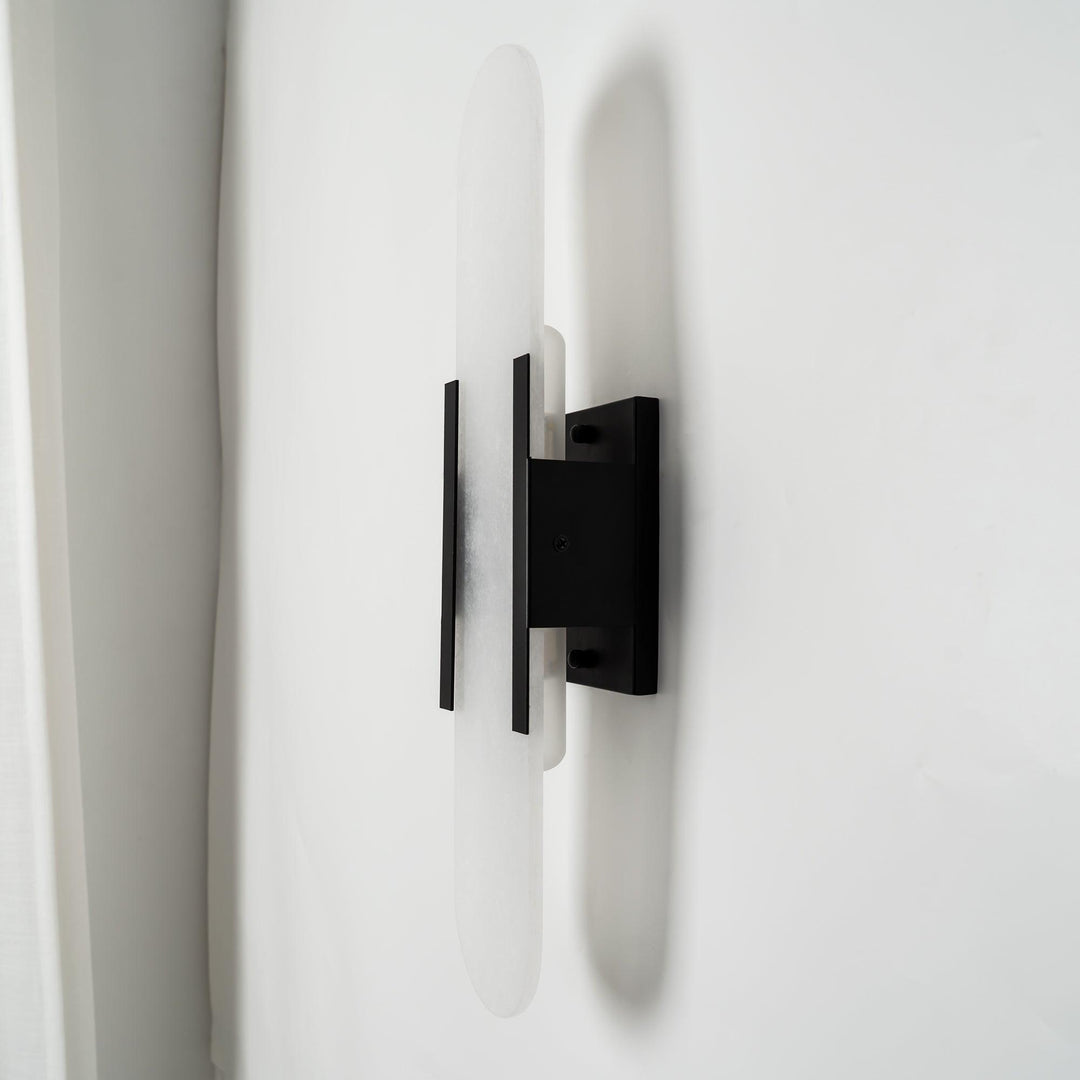"Modern elongated alabaster wall lamp with metal and brass accents, emits warm glow, suitable for chic interior decor."