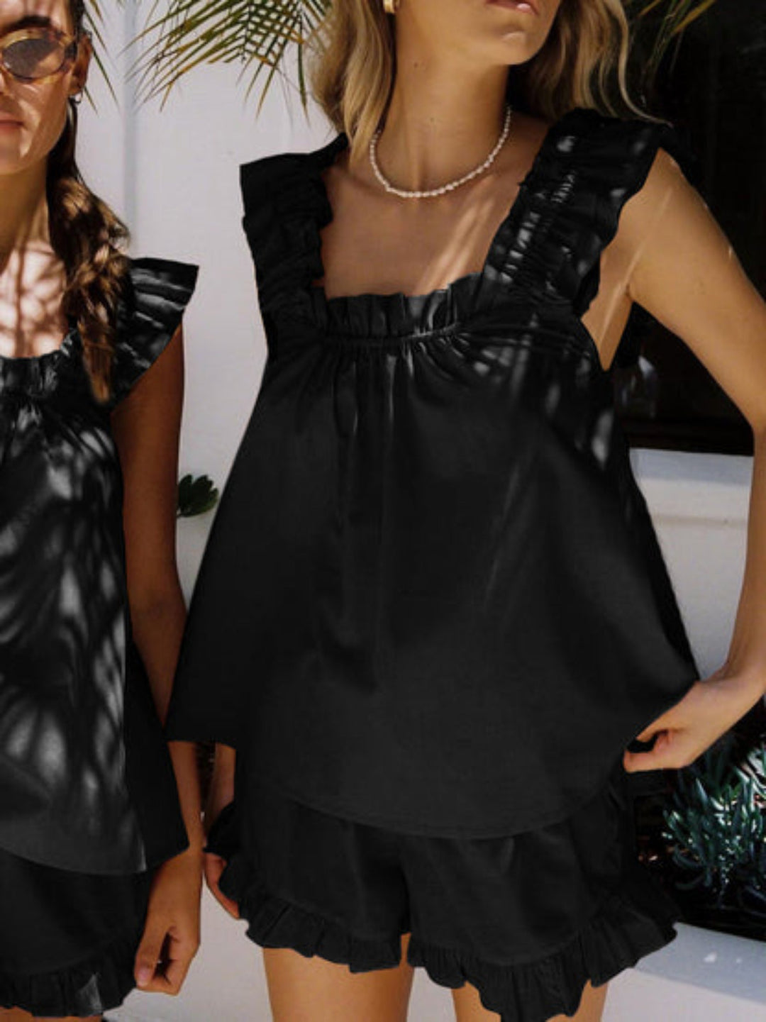 Woman wearing a comfortable ruffle summer pajama set. Sleeveless top and shorts for light, feminine sleepwear & loungewear.